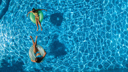 Aerial top view of children in swimming pool from above, happy kids swim on inflatable ring donuts and have fun in water on family holiday vacation on resort
