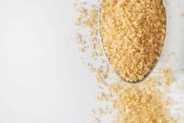 A part of metal spoon with brown sugar on the light background with copy space. Top view, closeup, selective focus.
