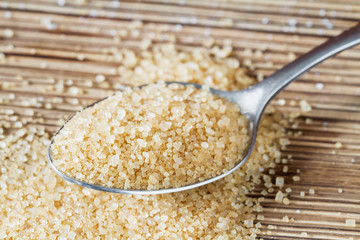 Brown sugar in metal spoon on the brown wooden background. Closeup, selective focus.