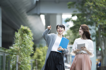 タブレットと資料を持ちながら外を歩いているOL