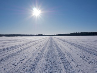Fototapeta na wymiar Frozen lake with snow mobile tracks crossing