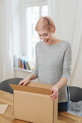 Pleased young woman opening a brown cardboard box