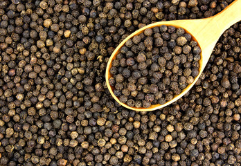 Black peppercorn seeds background with a wooden spoon