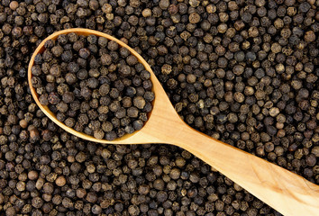 Black peppercorn seeds background with a wooden spoon