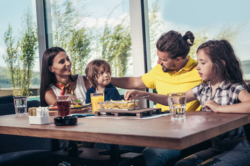 Father and mother with children enjoying meal in restaurant.