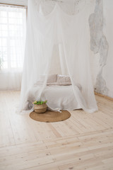 Fototapeta na wymiar Double bed with gray bed linen and canopy. Bedroom. A wicker chair made of wood in the corner of the room.