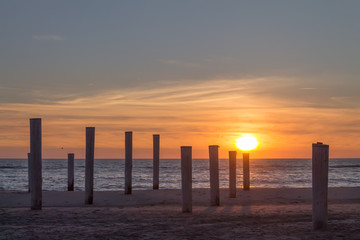 Fototapeta premium Wooden piles on an empty beach and a beautiful sunset sky over the sea, Petten, Holland,North Sea