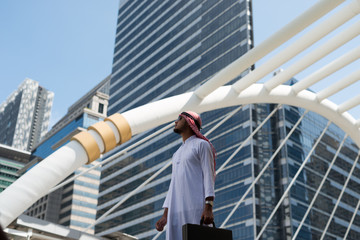 Young Arab businessman holding a bag standing in the city. in the background of bangkok city,  the business district with high building dazzled.