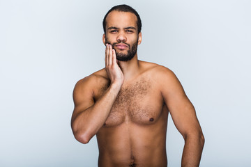 Toothache. Portrait of handsome shirtless young black man looking at camera and touching his chin while standing against white background