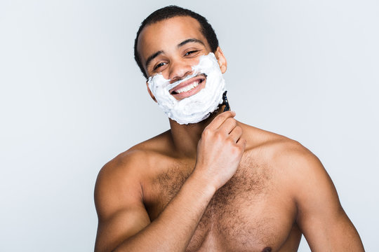 Bye Bye Beard! Handsome Shirtless Young Black Man Shaving While Standing Against White Background