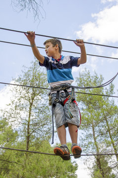 Leisure and activities on nature. Small boy hanging and walking on cables between trees.