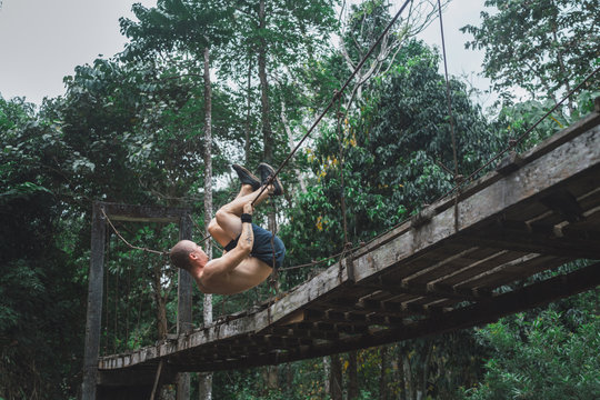 Man hanging on rope of bridge