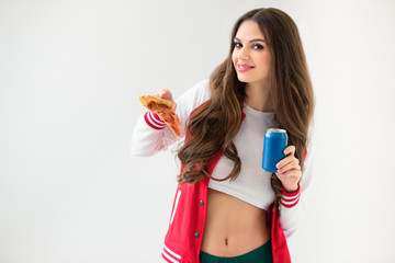 smiling sexy girl in baseball jacket holding pizza and can isolated on white