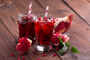 Ripe pomegranate seeds, fruit, and juice on brown wooden background