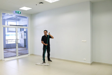 Asian male janitor mopping floor in walkway office building. Commercial Cleaning Services concept.