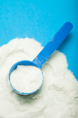Measuring spoon with milk powder on a blue background.