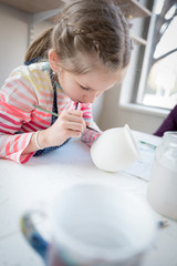 Young girl in pottery workshop decorating a cup