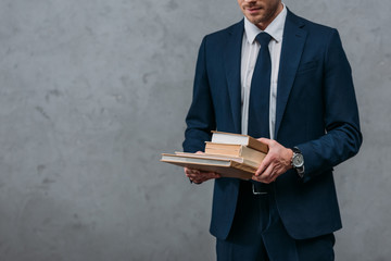 cropped shot of businessman holding stack of books in front of concrete wall