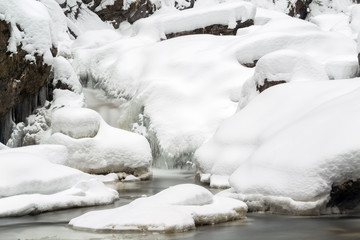 Stunning winter landscape, stones on wintry river covered snow and small waterfall