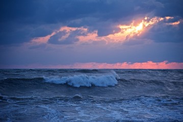 Storm at sunset. Big waves incoming. Golden sun rays between dark clouds. Stormy weather in the sea.