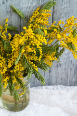 Mimosa twigs with blooming flowers in a glass jar near a wooden background