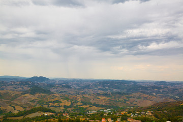 Panoramic view of San Marino. Green valley with orange roofs houses. Cloudly sky in summer.