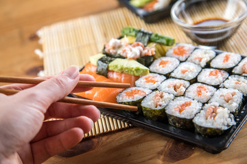 Weibliche Hand nimmt  Lachs Sushi Nigiri mit Stäbchen aus Bento Box mit Sojasauce