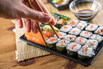 Frau isst Lachs Sushi Nigiri mit Stäbchen aus Bento Box mit Sojasoße
