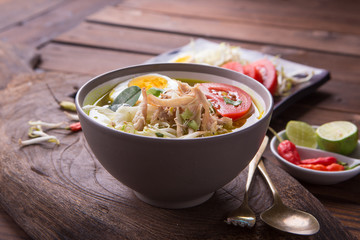 Soto: Indonesian chicken soup with hard boiled eggs, tomato, bean sprout, lemon, cayenne pepper on rustic brown wooden background