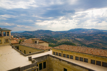 Fototapeta na wymiar San Marino. Beautiful view to the mountains behind houses with orange roofs. Summertime, Italy. Cloudly sky, heavy clouds.