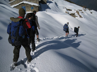 Hikers trekking in the Himalayas cast long shadows in the early morning as they make fresh foot...