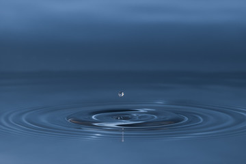 Fototapeta na wymiar drop of water liquid with splash isolated. the drop explodes in the water sending spray to the sides and circle ripples around it. the water is blue