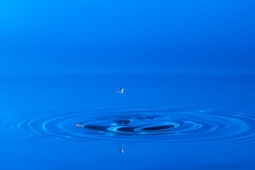 drop of water liquid with splash isolated. the drop explodes in the water sending spray to the sides and circle ripples around it. the water is blue