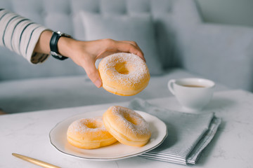 Food and Bakery, Hand Holding Delicious Fresh and Sweet Donut with Sugar Toppings on White Dish.