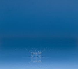 drop of water liquid with splash isolated. the drop explodes in the water sending spray to the sides and circle ripples around it. the water is blue