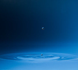 drop of water liquid with splash isolated. the drop explodes in the water sending spray to the sides and circle ripples around it. the water is blue