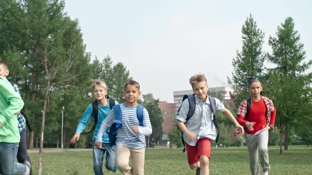 Front view of six primary school boys with backpacks running towards camera in park and smiling