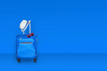 Blue suitcase with a summer hat and fashionable  sunglasses on light blue background, a summer...