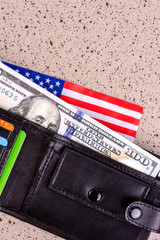 One hundred dollars banknote reach out out of a black old purse. And also part of the American flag. Vertical.