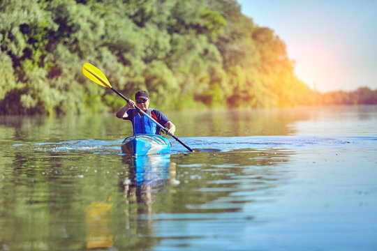  Man paddling a kayak on summer day.