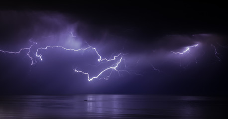 lightning bolts reflection over the sea. taken during a thunderstorm over the ocean with clouds in...