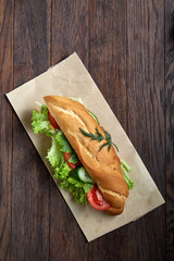 Fresh and tasty sandwich with cheese and vegetables on paper plate over wooden background,...