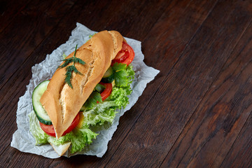 Fresh and tasty sandwich with cheese and vegetables on paper napkin over wooden background, selective focus, top view