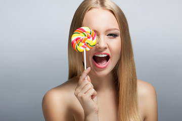 Cute young woman looking into the camera and holding a lollipop. Positive human emotions. Laugh