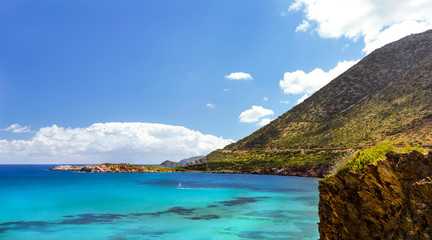 Windsurf with red sail rides on sea on background rocky mountain. View from Livadi beach in resort village Bali. Rethymno, Crete Greece. Extreme water sports as active recreation on Sunny vacations