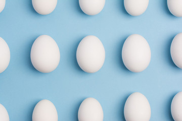 Happy Easter concept. Pattern of white eggs on blue background close up. Flat lay. Minimal concept. Top view. Design, visual art.