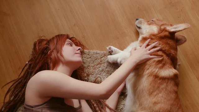 Young pretty woman with red dreadlocks having good time with corgi dog 
