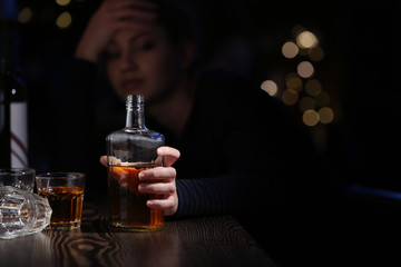 Young woman with bottle of drink in bar. Alcoholism problem