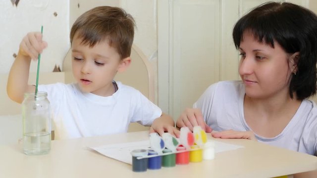 The child and mother paint with watercolor on a white sheet of paper.