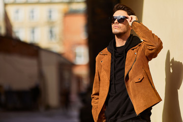 Model looking man stand near the wall and hold his glasses towards the sun shine